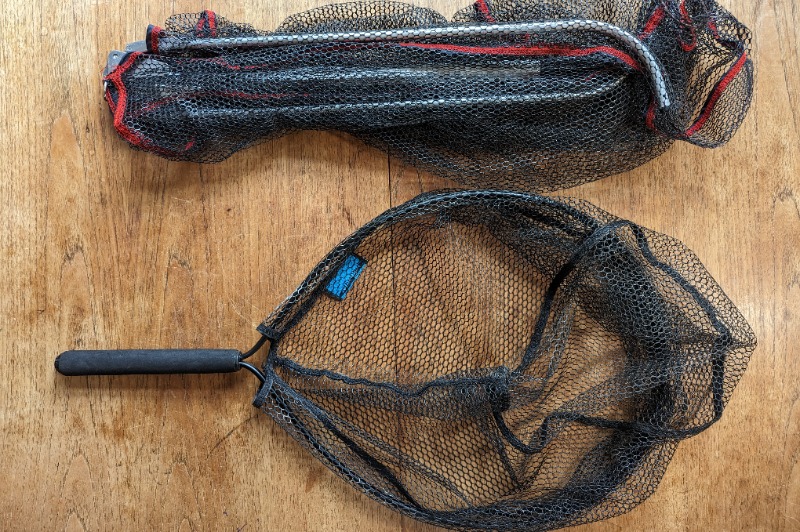 A trout fishing net and a folding net laid on a wooden table