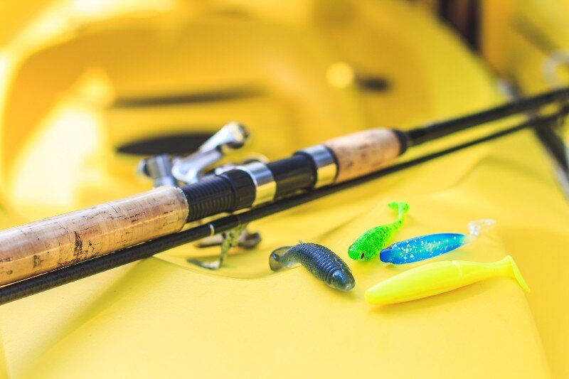 A yellow kayak with a cork handled fishing rod and lures on top