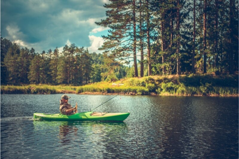 A man fishing from a kayak in a lake near a pine forest