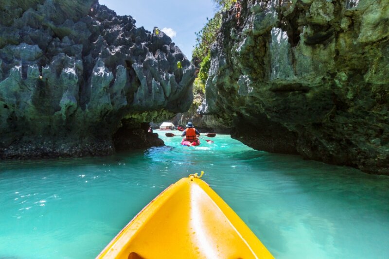 A yellow kayak sneaking between two rocks in a turquoise sea