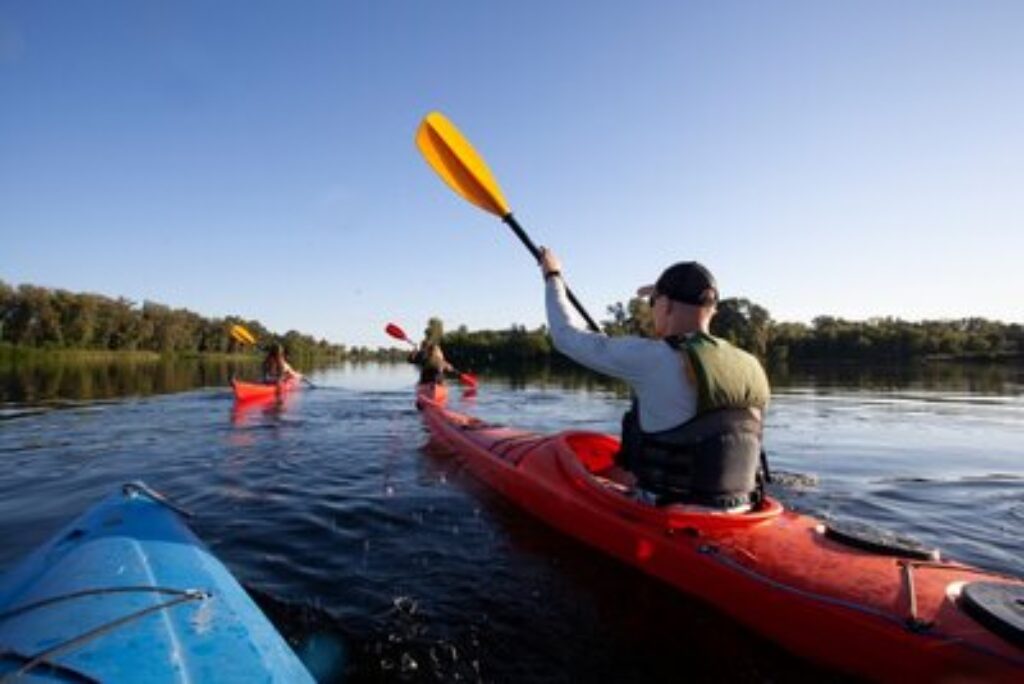 A man paddling in a sit-in kayak on a lake with two others