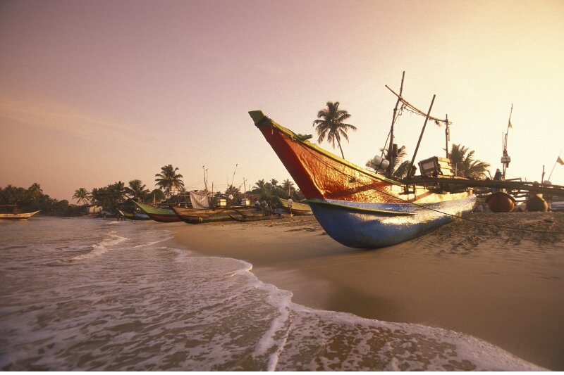 A beach in Sri Lanka with a fishing boat on it at sunrise