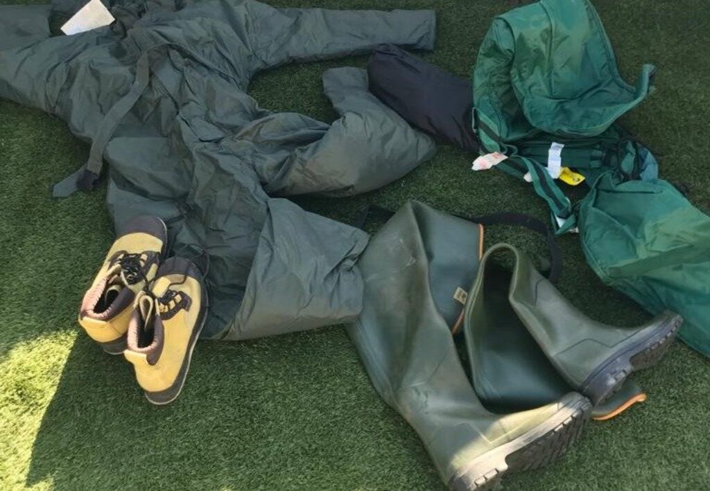 Waders, a wading fishing suit and fishing boots laid out on astro turf